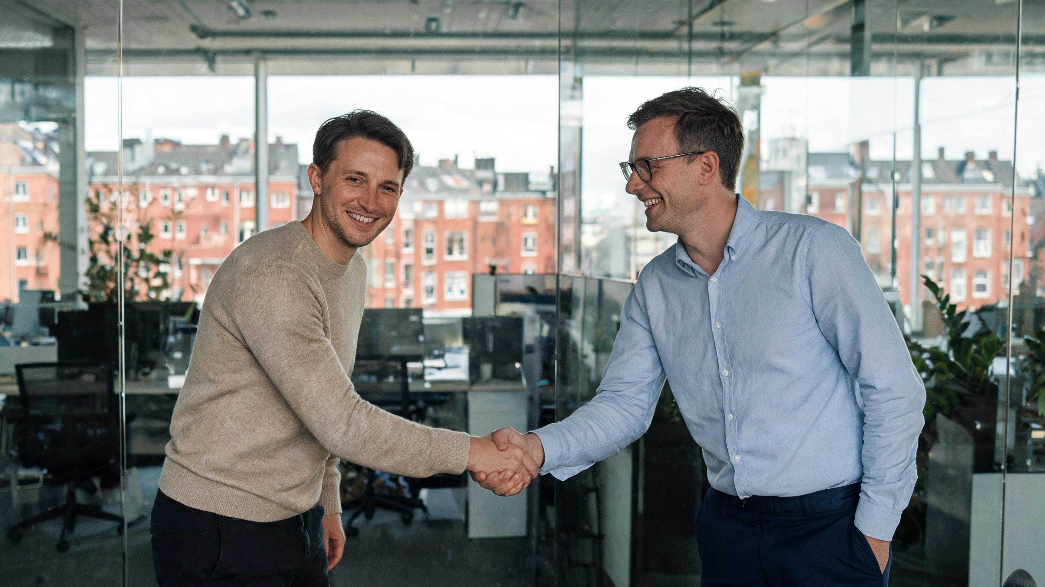 Um recrutador e um candidato a emprego apertando as mãos em um escritório amplo e iluminado em Malmö, paredes de vidro, vista da cidade com prédios de tijolos vermelhos ao fundo, ambos vestindo trajes smart-casual.
